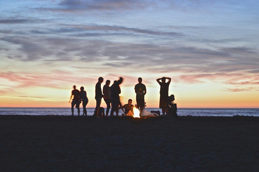 Grupo de personas reunidas alrededor de una fogata en la playa al atardecer, compartiendo un momento mágico.