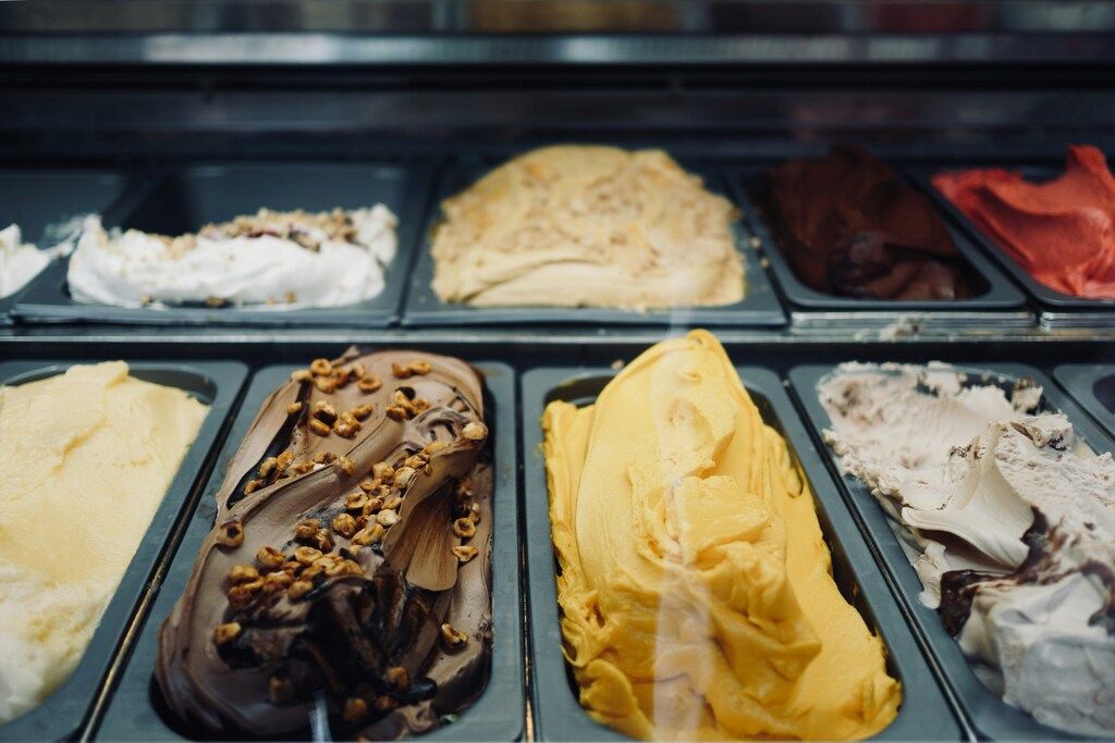 Una vitrina de heladería con varias bandejas de gelato artesanal de diferentes sabores, incluyendo chocolate con avellanas, pistacho, y vainilla.