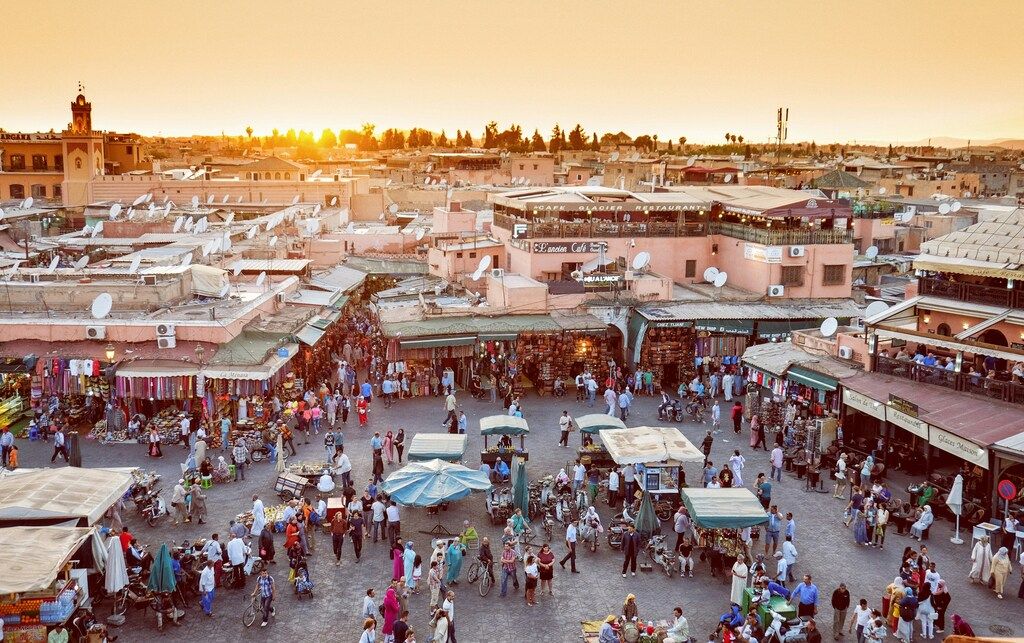 Vista panorámica de la plaza Jemaa el-Fna en Marrakech llena de gente y puestos al atardecer.
