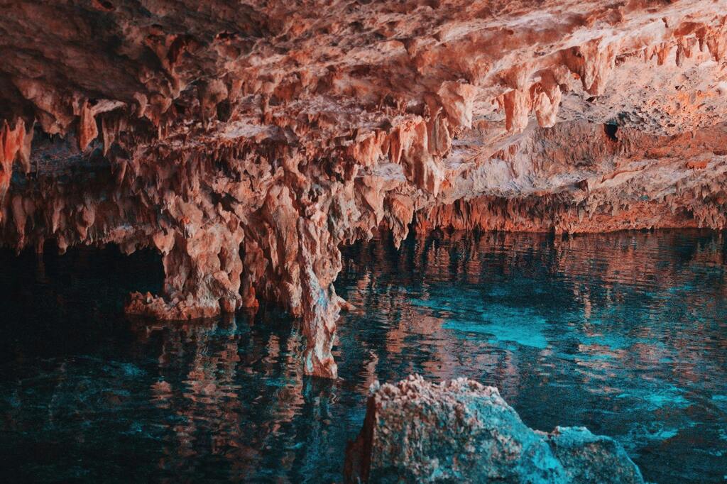 Formaciones rocosas y estalactitas dentro de un cenote, reflejadas en aguas turquesa.