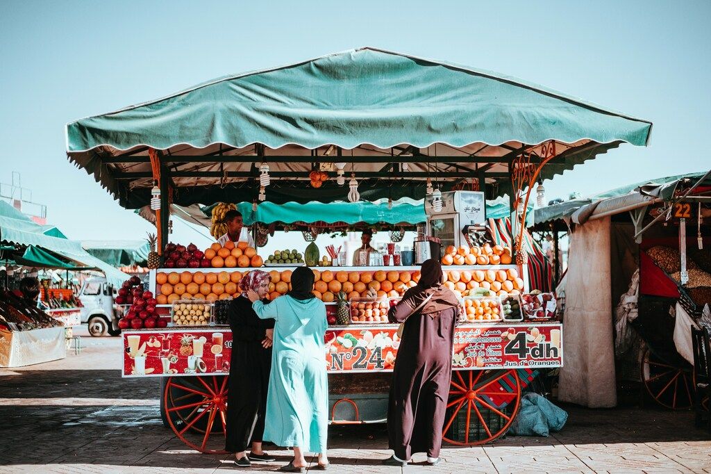 Puesto callejero de jugos con frutas frescas y personas comprando en un mercado tradicional marroquí.