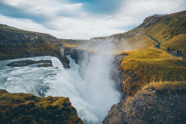 Espectacular vista de la cascada de Gullfoss en Islandia, con un cañón brumoso y laderas cubiertas de hierba amarilla.