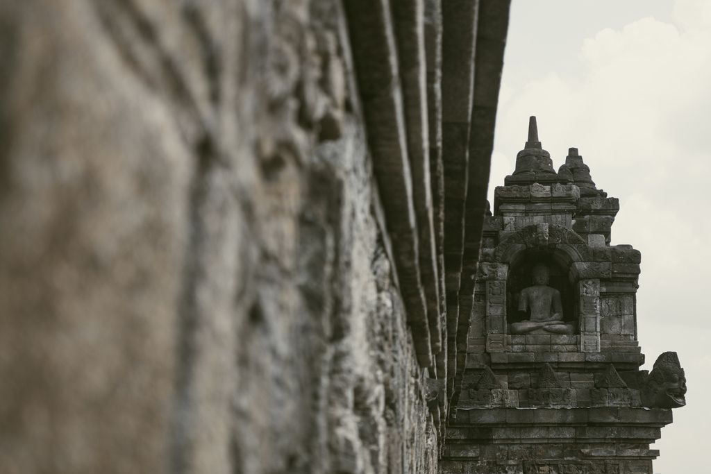 Detalle de una estatua de Buda en una de las torres del templo de Borobudur, con enfoque lateral en las piedras del monumento.