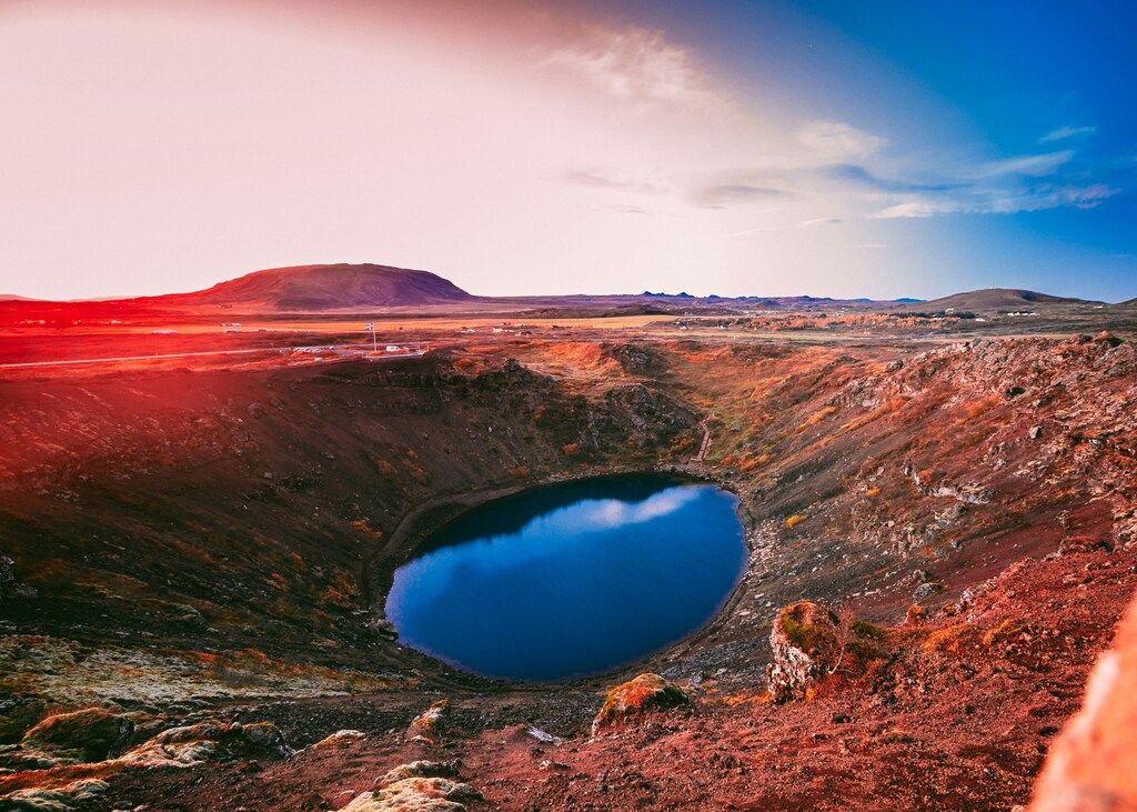 El cráter volcánico Kerið con un lago azul en el centro, rodeado de tierra rojiza y paisaje islandés.