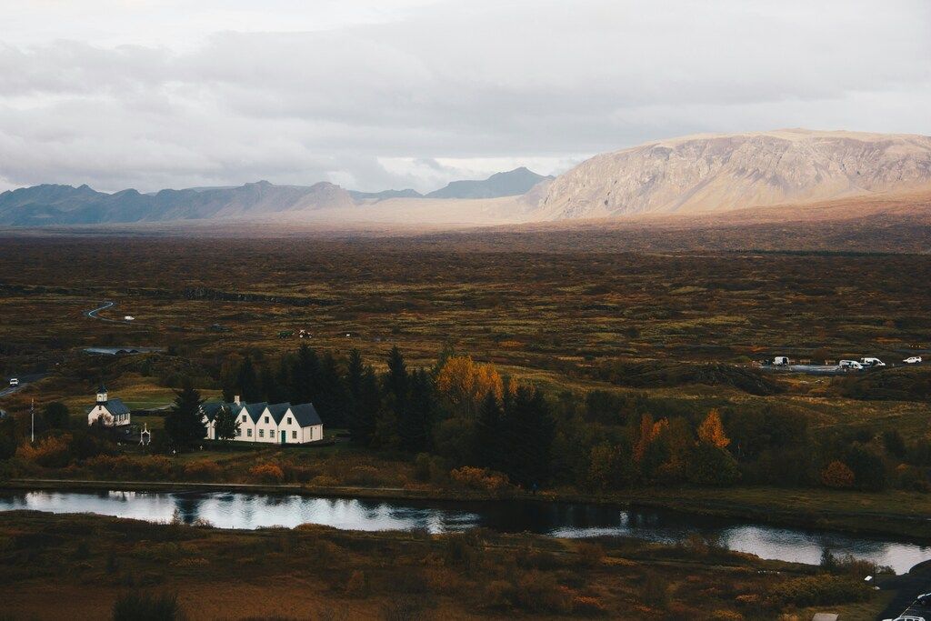 Vista panorámica del Parque Nacional Þingvellir con casas blancas, árboles otoñales y montañas al fondo en Islandia.