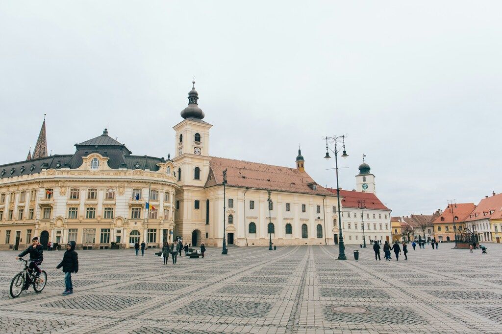 Plaza principal de Sibiu con edificios históricos y gente paseando, en un día nublado.