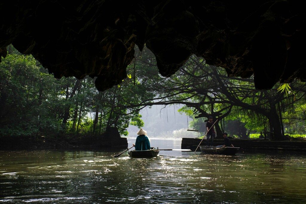 Botes remando a través de una cueva fluvial en el paisaje natural de Tam Coc.