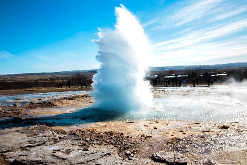 Erupción del géiser Strokkur lanzando una columna de agua al cielo bajo un cielo azul en la zona geotérmica de Haukadalur.