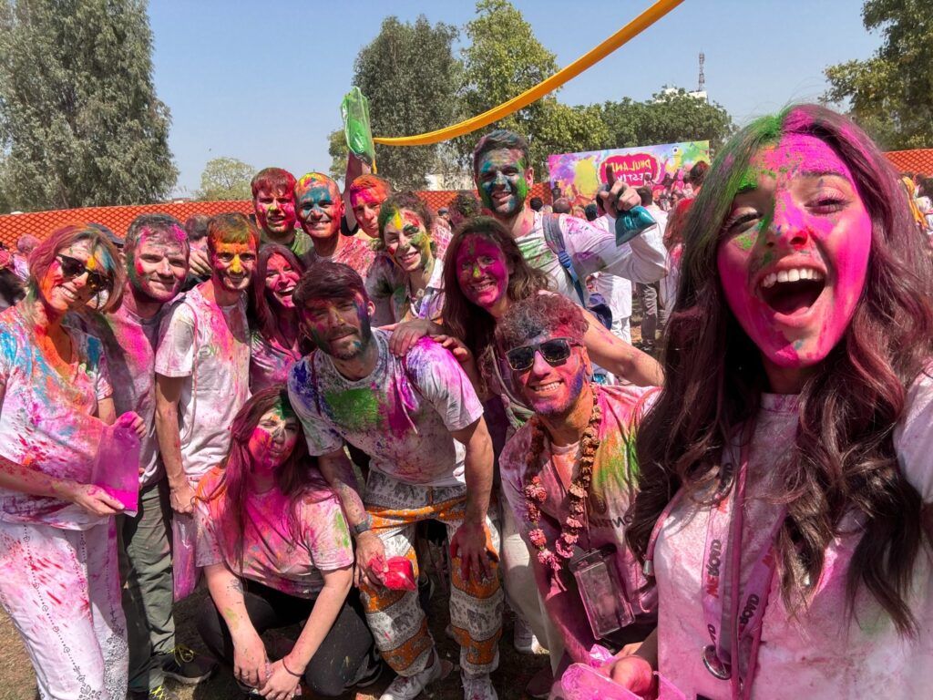 Grupo de viajeros WeRoad celebrando con alegría el festival Holi en India, cubiertos de vibrantes polvos de colores.