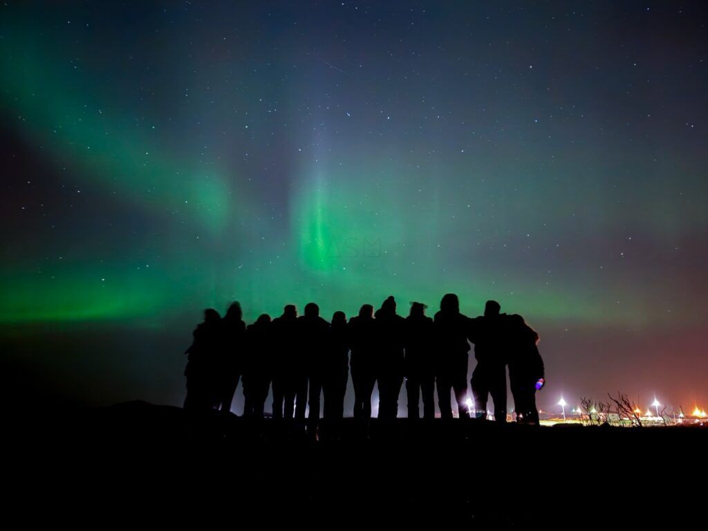 Grupo de viajeros mirando la aurora boreal sobre el cielo nocturno de Islandia.