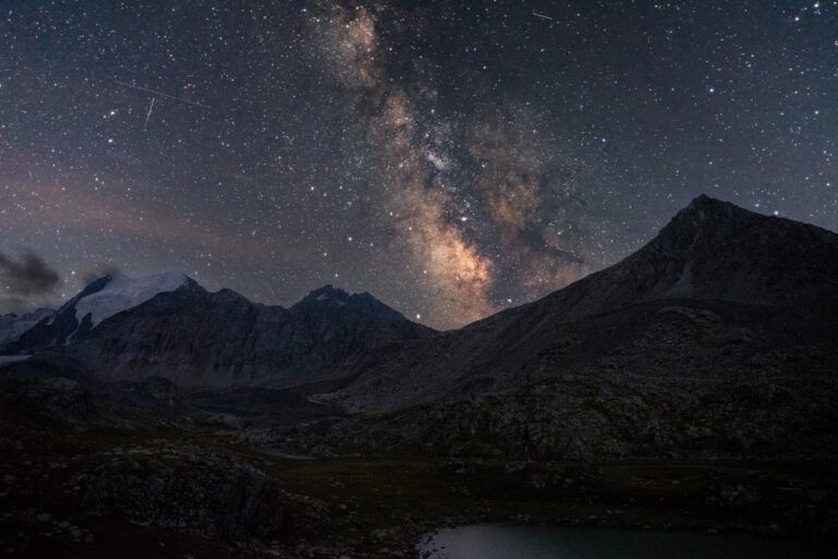 Un paisaje de Kirguistán con la Vía Láctea brillando sobre un valle de montañas y un lago al anochecer.