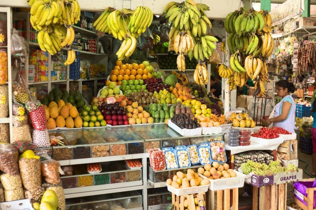 Puesto de mercado lleno de diversas frutas frescas como plátanos, mangos y uvas.
