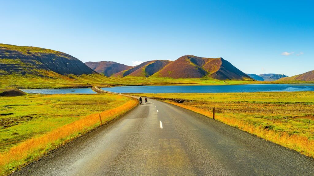 La Ring Road de Islandia y un paisaje de verdes colinas y un lago azul bajo un cielo despejado.