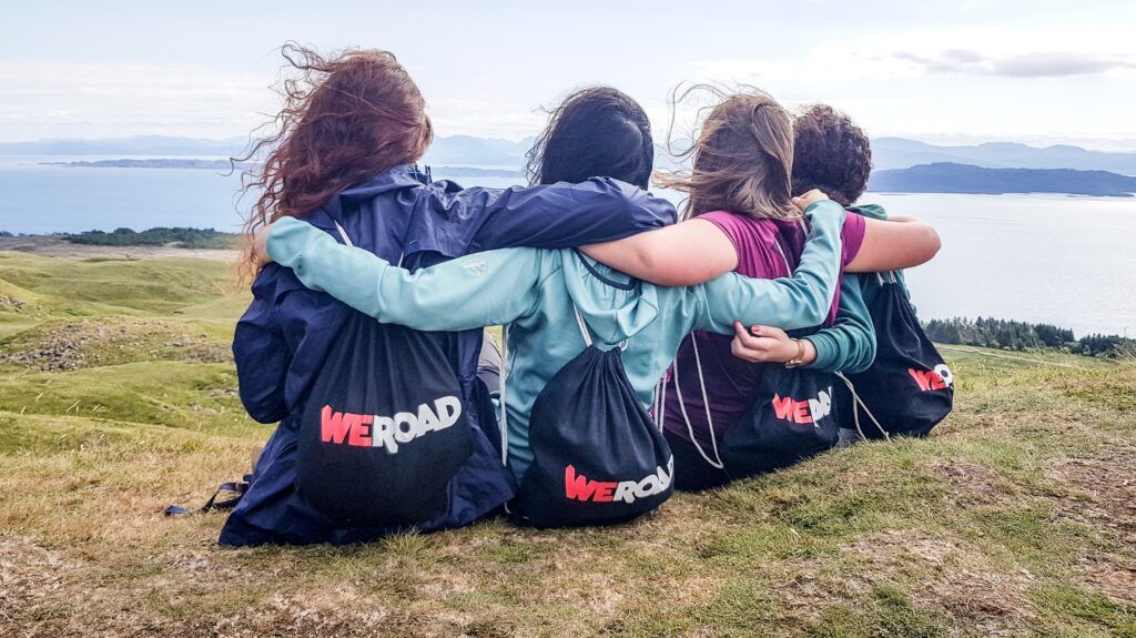Grupo de viajeros abrazados mirando el horizonte durante un viaje de grupo de WeRoad en Escocia.