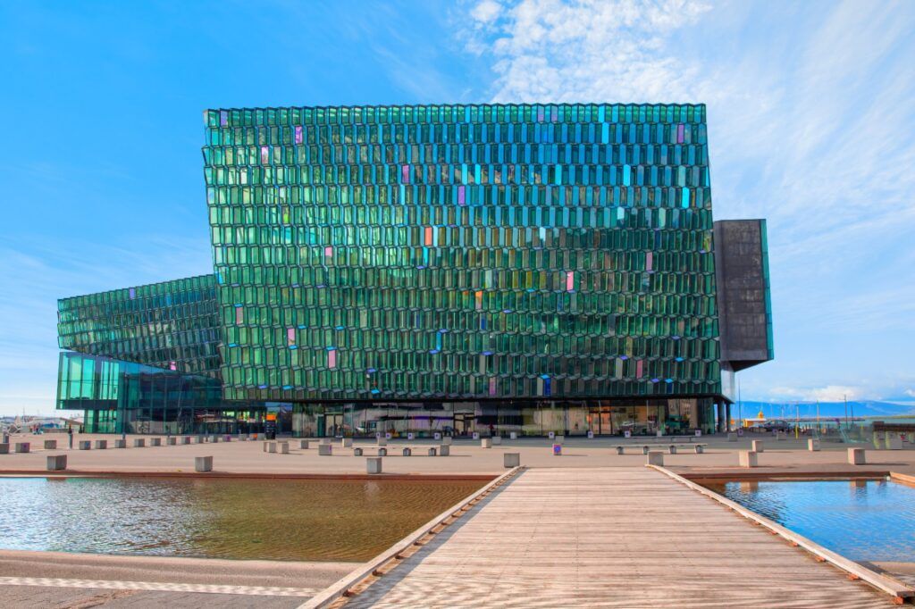 Fachada de cristal hexagonal y de color verde del Centro de Conciertos Harpa en Reikiavik, con estanques en primer plano.