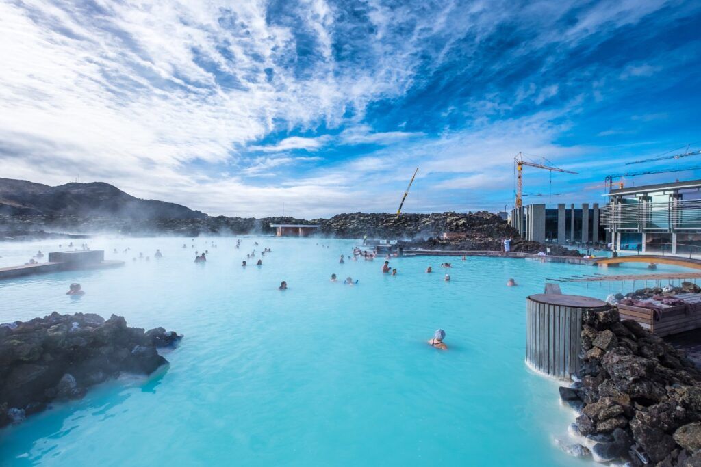 Gente bañándose en la Laguna Azul (Blue Lagoon) geotermal de Islandia, con agua turquesa y vapor bajo un cielo azul.