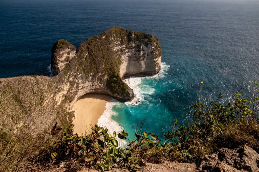 Vista aérea del acantilado Kelingking Beach en Nusa Penida, Bali, conocido como T-Rex Bay, con la playa de arena dorada y el agua turquesa.