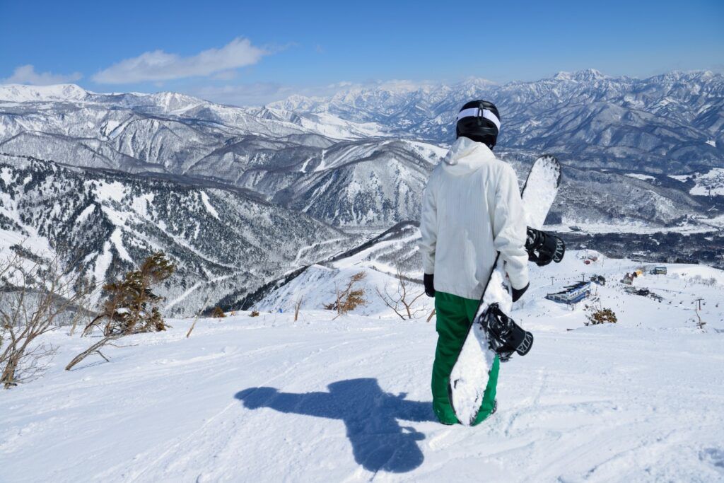 Snowboarder en la cima de una pista, con vista panorámica de los Alpes Japoneses.