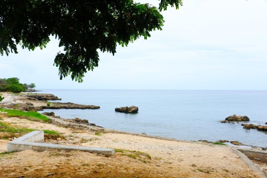 Costa rocosa y orilla de arena con un mar tranquilo bajo un cielo nublado, en Playa la Boca.