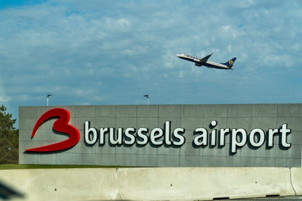 Avión de Ryanair despegando por encima del gran letrero exterior del Aeropuerto de Bruselas (Brussels Airport) contra un cielo nublado.