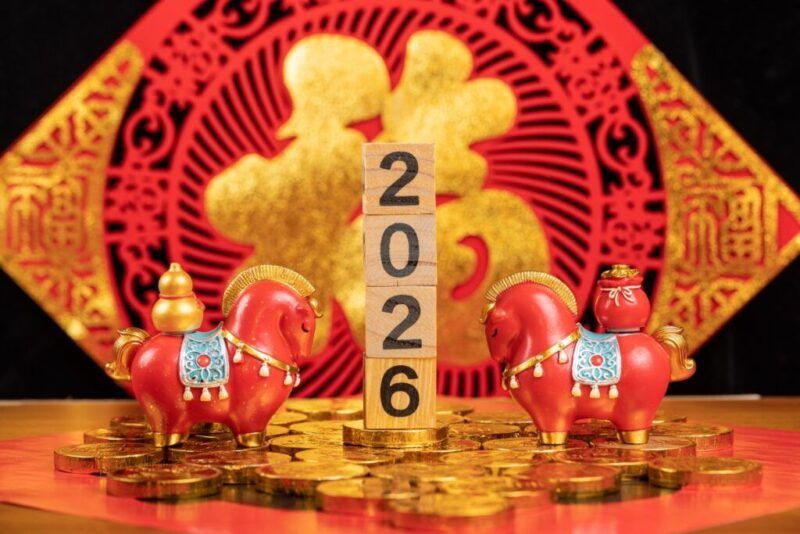Decoraciones para la celebración del Año Nuevo chino 2026 con bloques de madera que muestran el año, rodeados de figuritas de caballos rojos y monedas de oro.