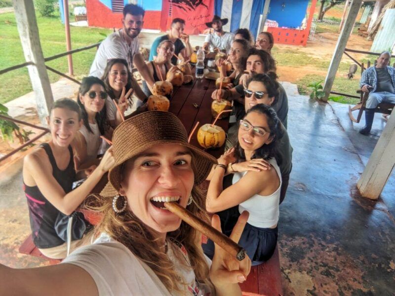 Una foto de un grupo de viajeros de WeRoad comiendo cocos y fumando puros bajo una cabaña en Cuba.