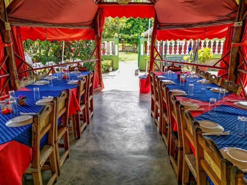 Largas mesas de comedor de madera con manteles azules para una comida en grupo en una terraza cubierta al aire libre en Cuba.