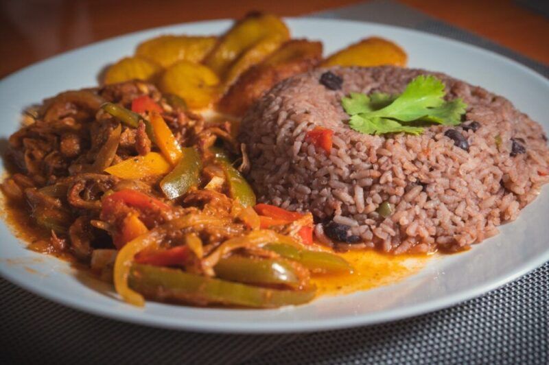 Un plato tradicional cubano de Ropa Vieja servido con Congri (arroz y frijoles negros) y plátanos fritos en un plato blanco.