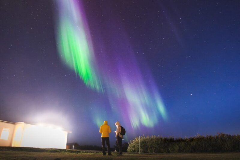 Dos personas observan una aurora boreal de color verde y violeta bajo un cielo estrellado en Islandia.