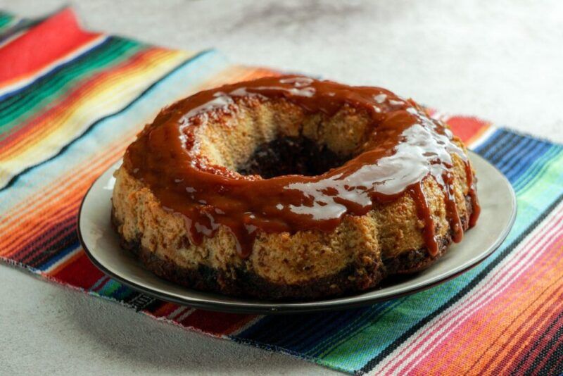 Un Chocoflan mexicano cubierto con salsa de caramelo y servido en una tela de zarape de rayas coloridas.