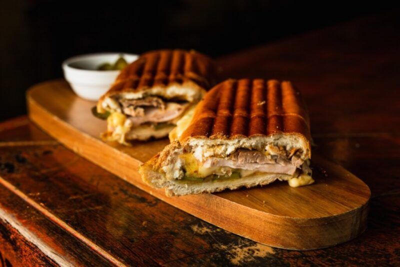 Un sándwich cubano en rodajas con cerdo asado, jamón, queso suizo y pepinillos en una tabla de madera.