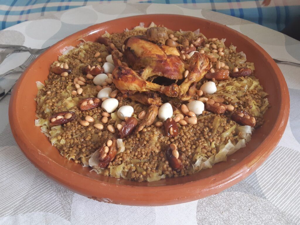 Gran plato tradicional de Rfissa marroquí servido en una fuente de barro, con pollo asado al centro rodeado de lentejas, huevos de codorniz, dátiles y frutos secos.