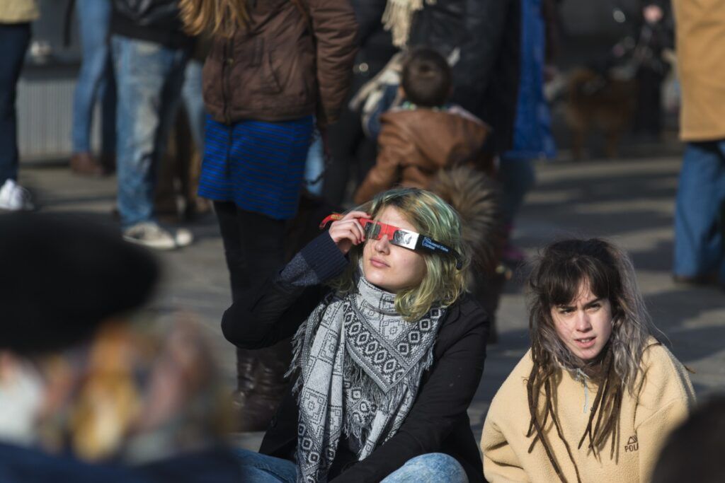 Una joven con gafas protectoras especiales observa un eclipse solar en una plaza pública en España.