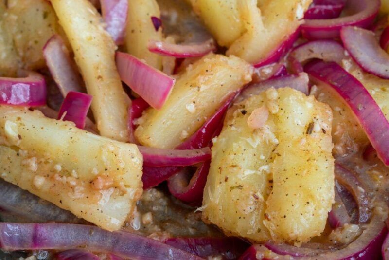Primer plano de la yuca con aliño cocida al estilo cubano, servida con cebollas rojas salteadas y ajo.