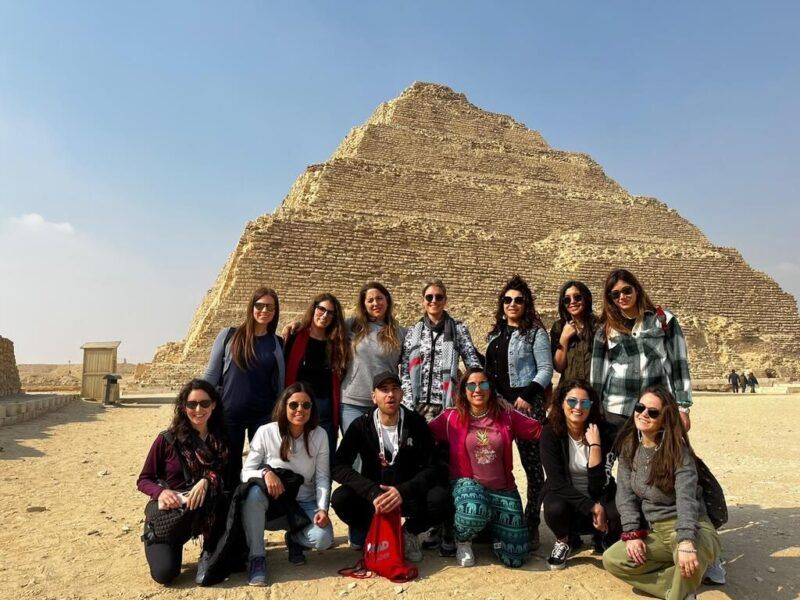 Un grupo de viajeros WeRoad posan frente a una pirámide escalonada en el desierto de Egipto.