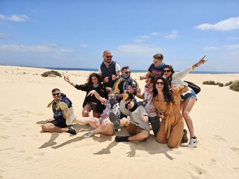 Un alegre grupo de viajeros de WeRoad posan en las dunas de arena de una playa egipcia bajo un cielo azul.