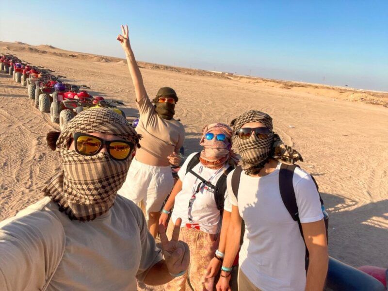 Un grupo de viajeros WeRoad con gafas de sol y gafas de sol posan frente a una fila de quads en el desierto egipcio.