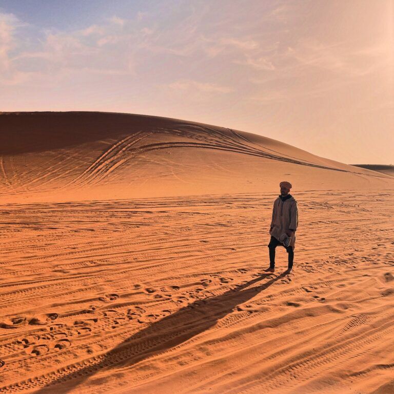 Un paisaje desértico inmenso con dunas de arena dorada onduladas bajo un cielo despejado al atardecer.