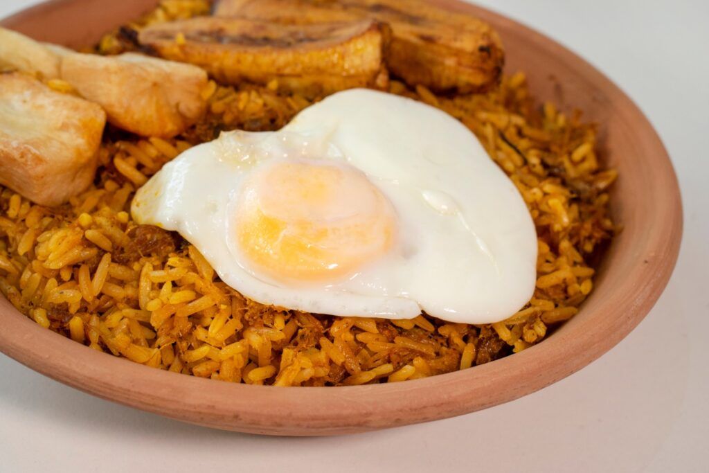 Un plato de majadito boliviano con arroz, carne, un huevo frito y plátano frito en un cuenco de barro.
