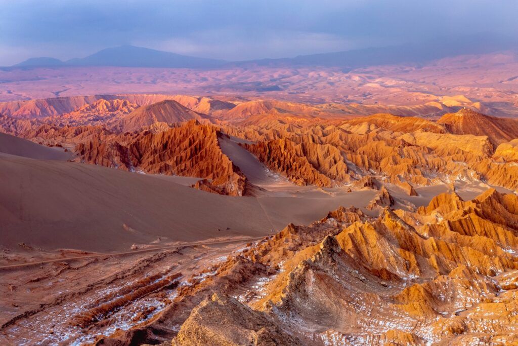 Una vista panorámica del Valle de la Luna en el desierto de Atacama, Chile, mostrando formaciones rocosas rojizas y dunas de arena bajo una luz suave.