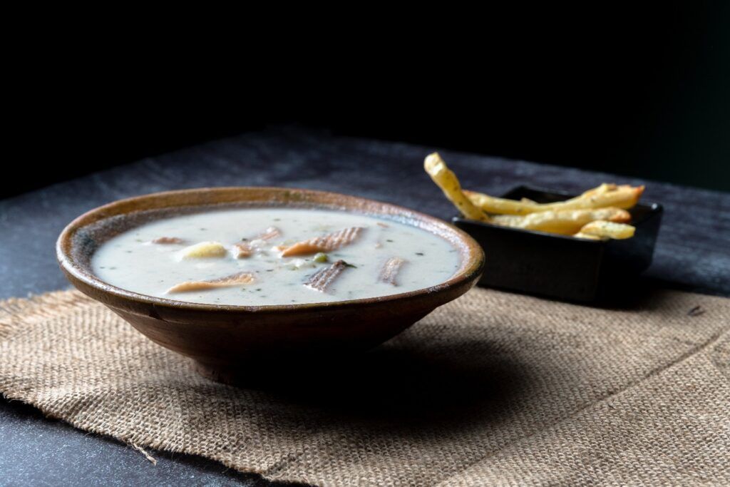 Un cuenco de barro con sopa de maní caliente servida sobre una mesa rústica, acompañada de papas fritas finas.