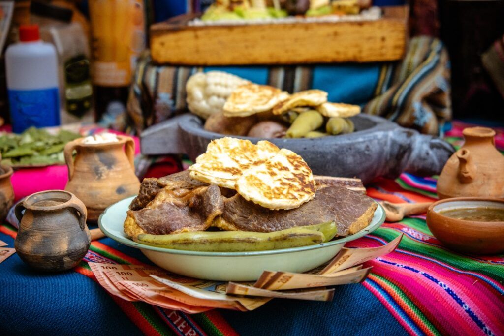 Un plato de carne asada servido con queso frito y vegetales sobre una mesa decorada con textiles tradicionales andinos.