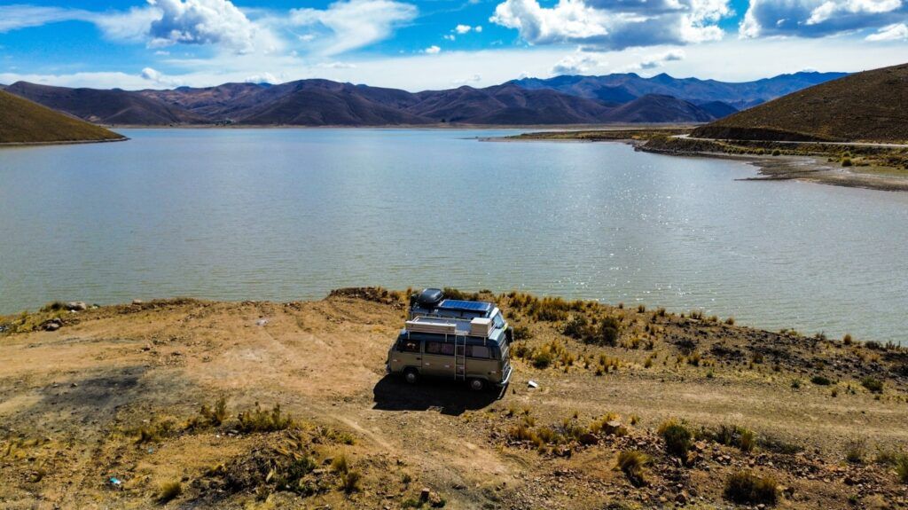 Una furgoneta camper aparcada frente a un gran lago rodeado de montañas en Challapata, Bolivia.