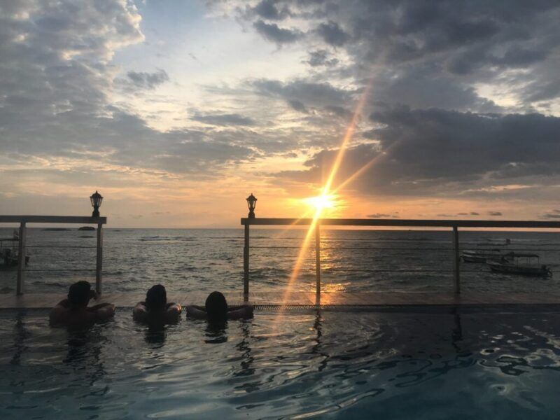 Tres personas disfrutan de la puesta de sol sobre el mar desde una piscina infinita en Sri Lanka.