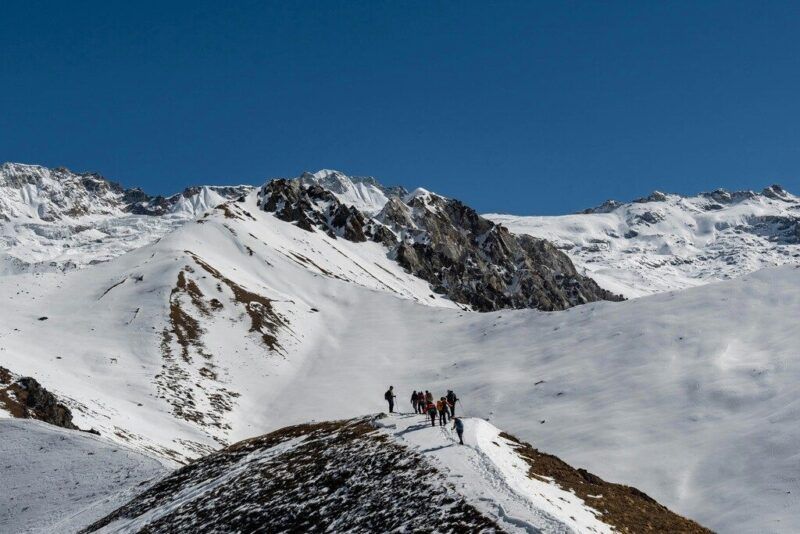 Caminantes en fila india por una cresta nevada con vistas panorámicas de los picos del Himalaya.