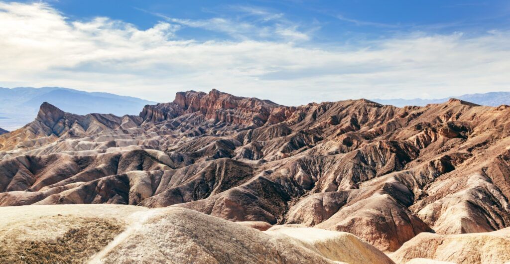 Vista panorámica de las áridas y onduladas formaciones rocosas de las tierras baldías bajo un cielo azul despejado en el Valle de la Muerte, California.