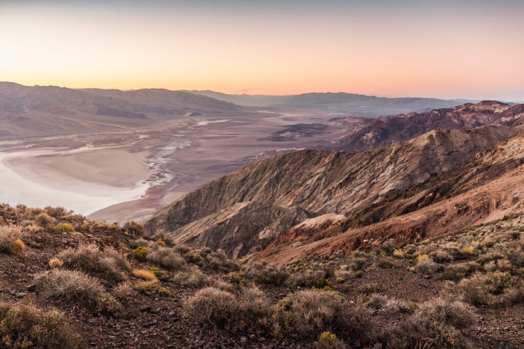Vista panorámica del valle desértico desde Dante's View al atardecer, con montañas áridas y salinas blancas bajo un cielo rosado.