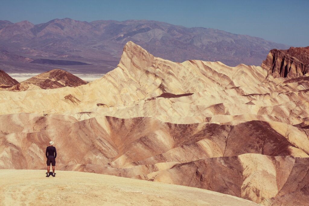 Un excursionista contempla desde una colina las vastas y onduladas formaciones rocosas de color ocre en Zabriskie Point, Valle de la Muerte.