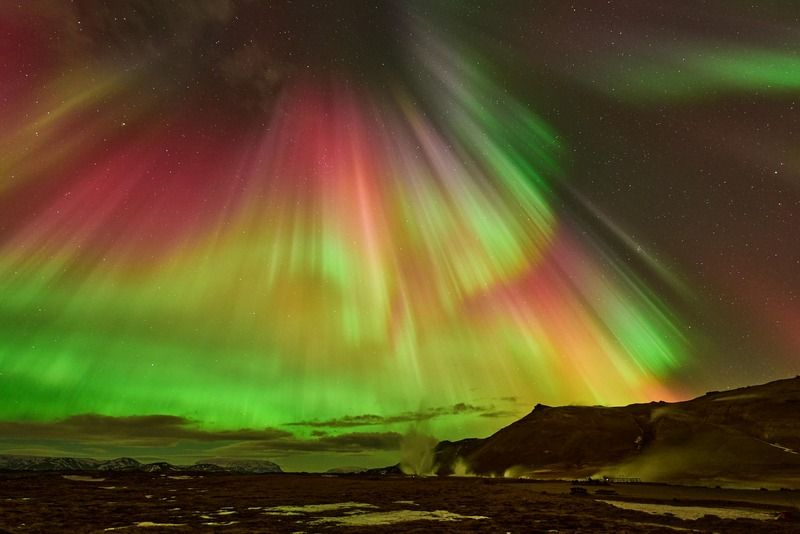 Aurora boreal con tonos rojos, verdes y amarillos sobre un paisaje montanoso nevado por la noche