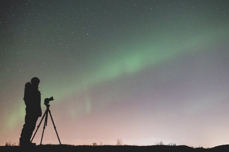 Silueta de un fotografo con tripode capturando la aurora boreal verde bajo un cielo estrellado nocturno